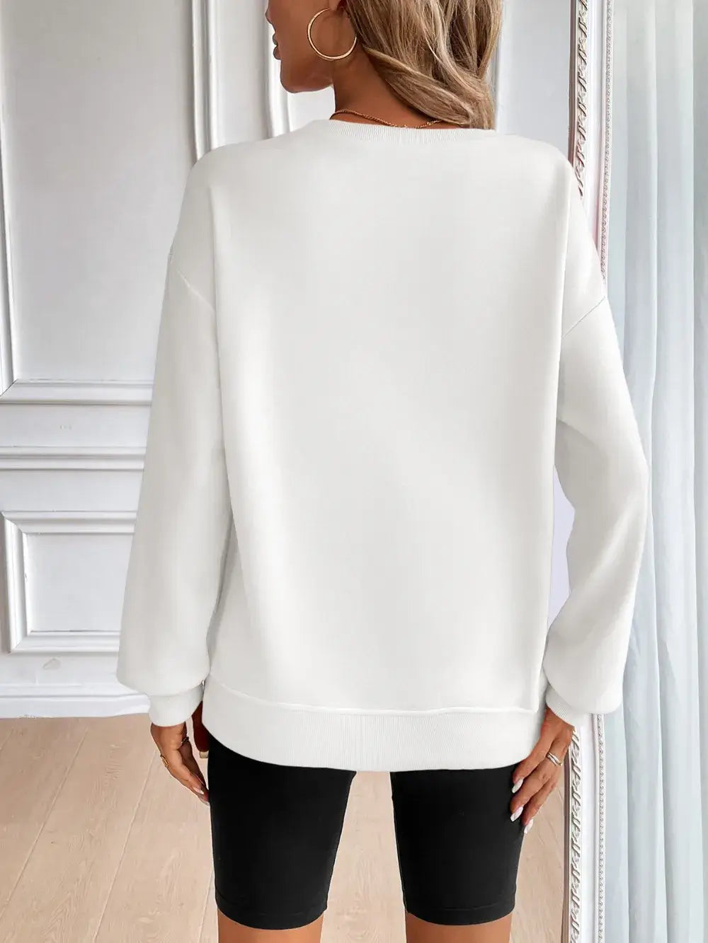 Back view of a woman wearing a white Ivy Lane round neck long sleeve sweatshirt with black shorts.