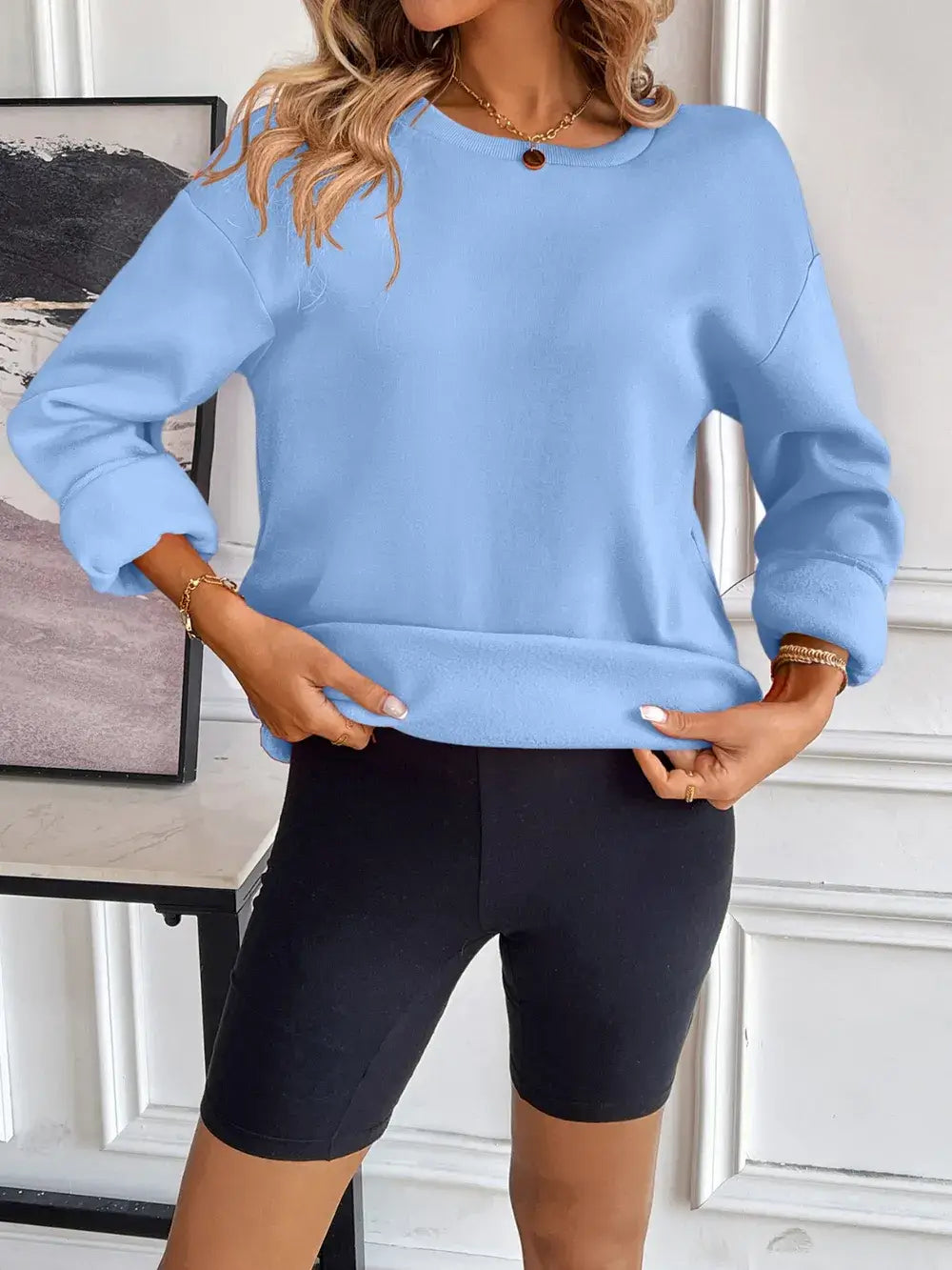 Model wearing a blue Ivy Lane round neck long sleeve sweatshirt with black shorts.
